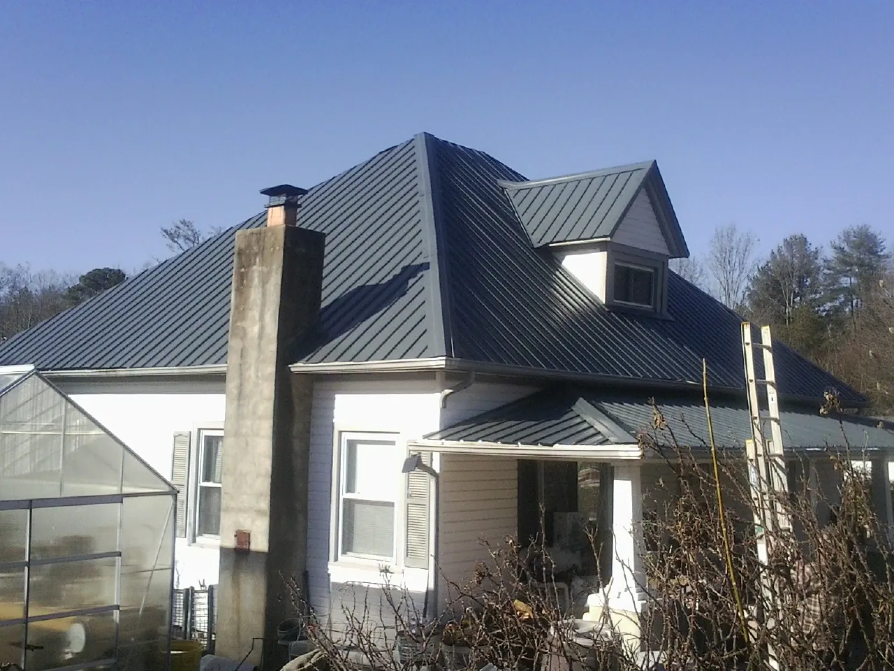 Dark blue standing seam metal roof on a white farmhouse with dormer — Slate & Tile Roof Repair by Roofing Brothers in Otis