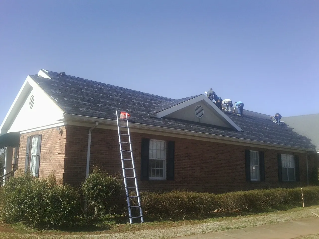 Crew tearing shingles off a brick ranch roof with a ladder set — Metal Roof Repair work by our crew in Otis