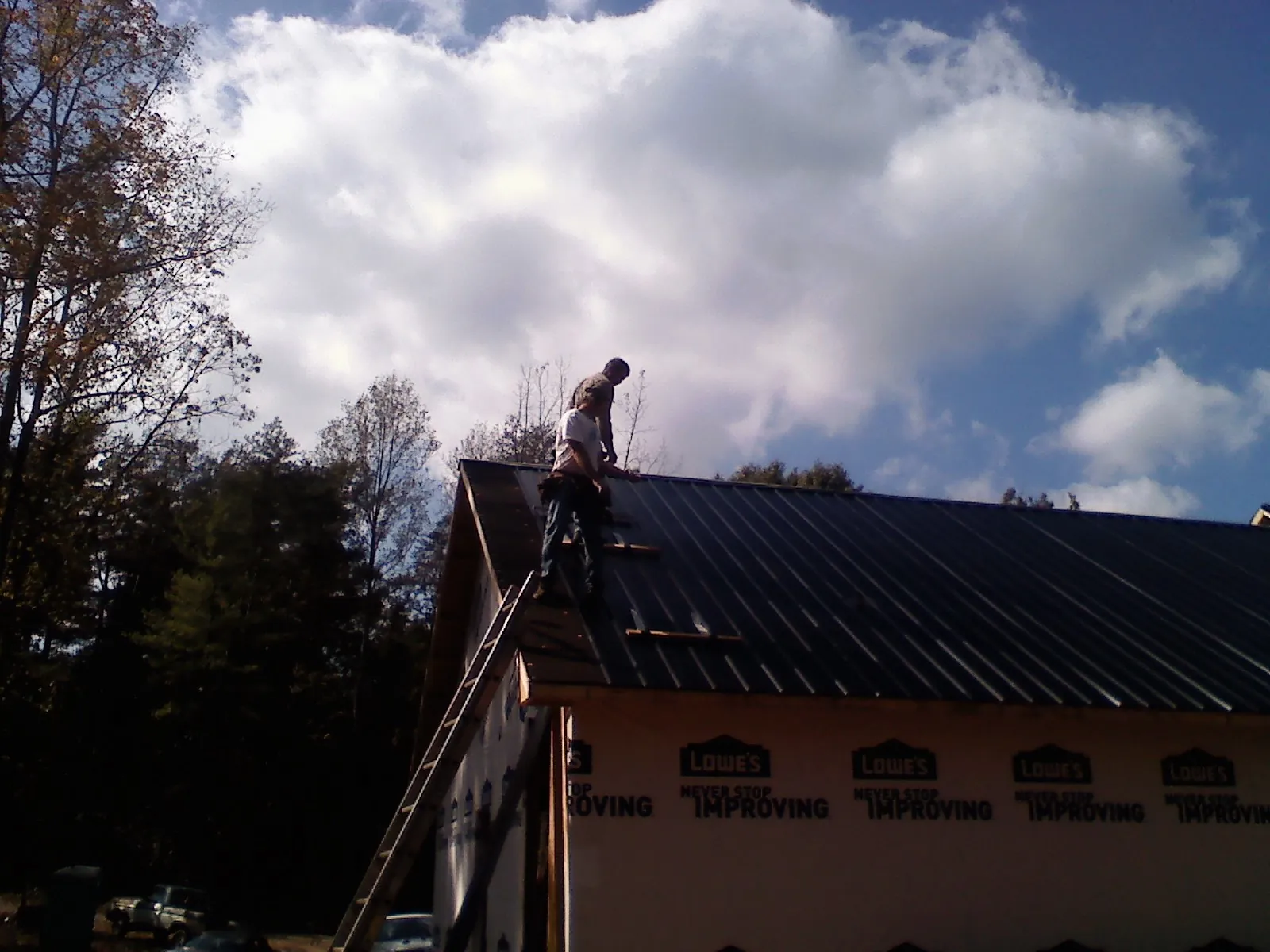 Roofer fastening dark metal panels high against a cloudy sky, from a Roof Inspection job in Otis