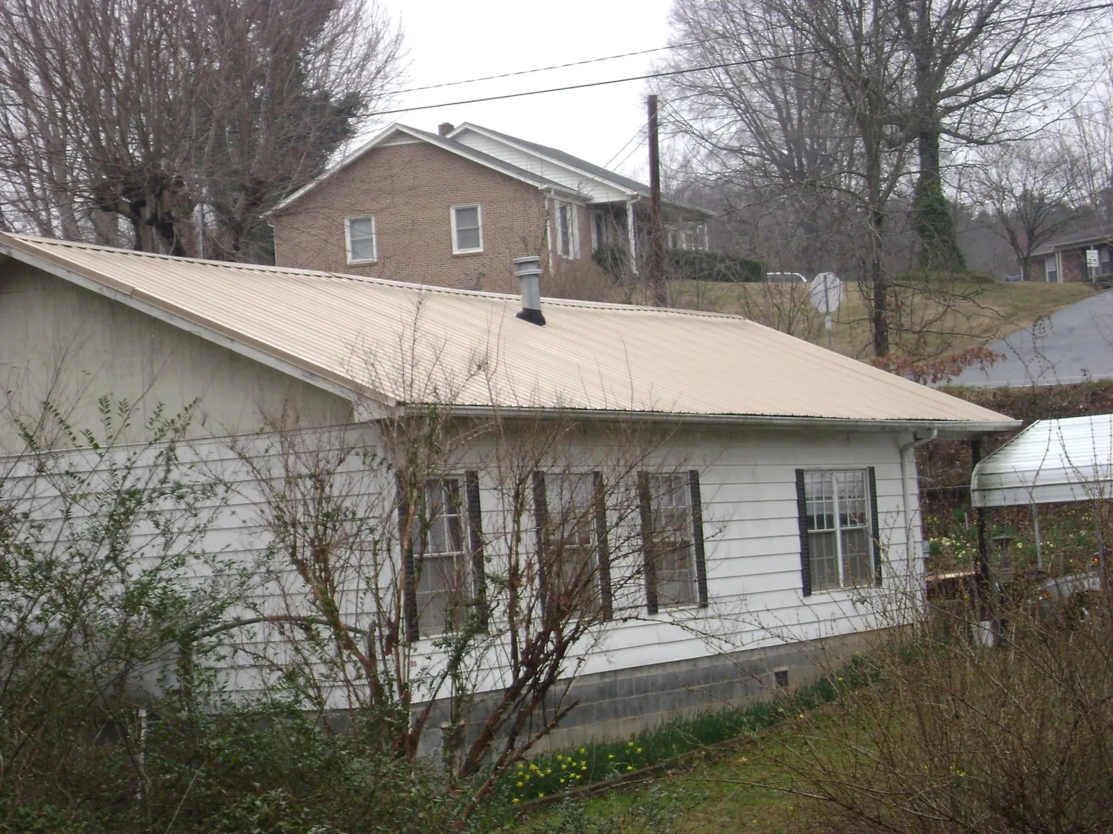 Tan metal roof on a white sided house set into a hillside — Commercial Roofing by Roofing Brothers in Otis