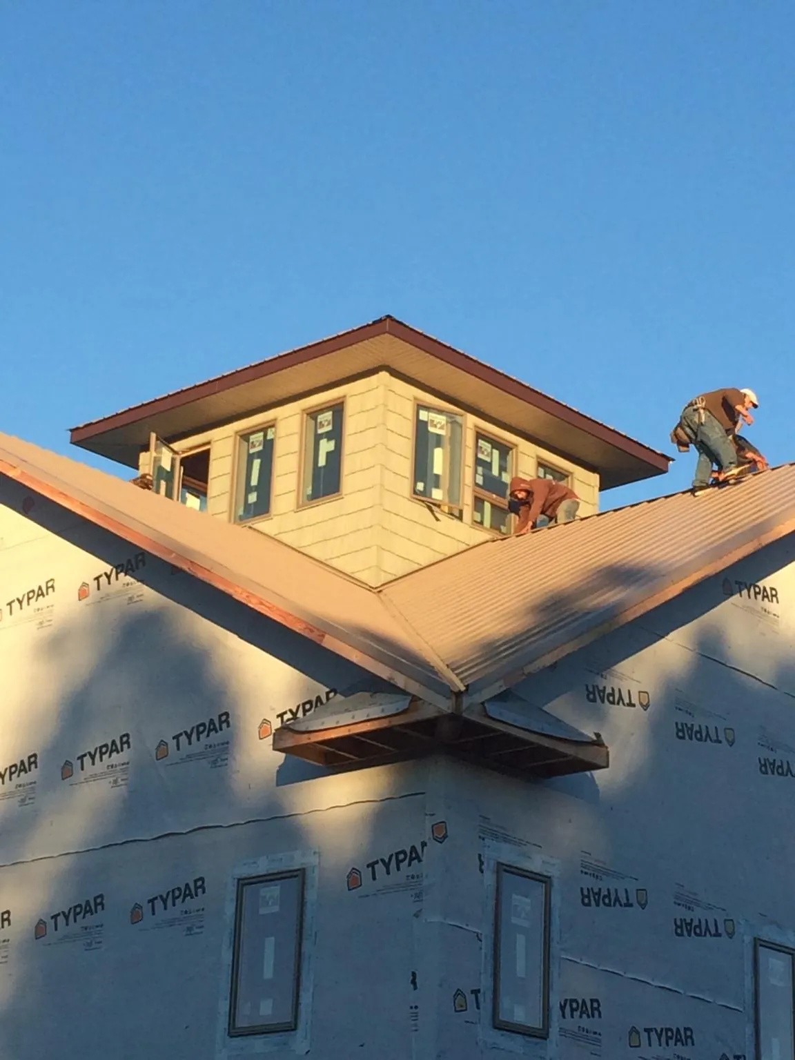 Roofers working around a rooftop cupola on a new metal roof at sunset — Roof Waterproofing in Otis by Roofing Brothers